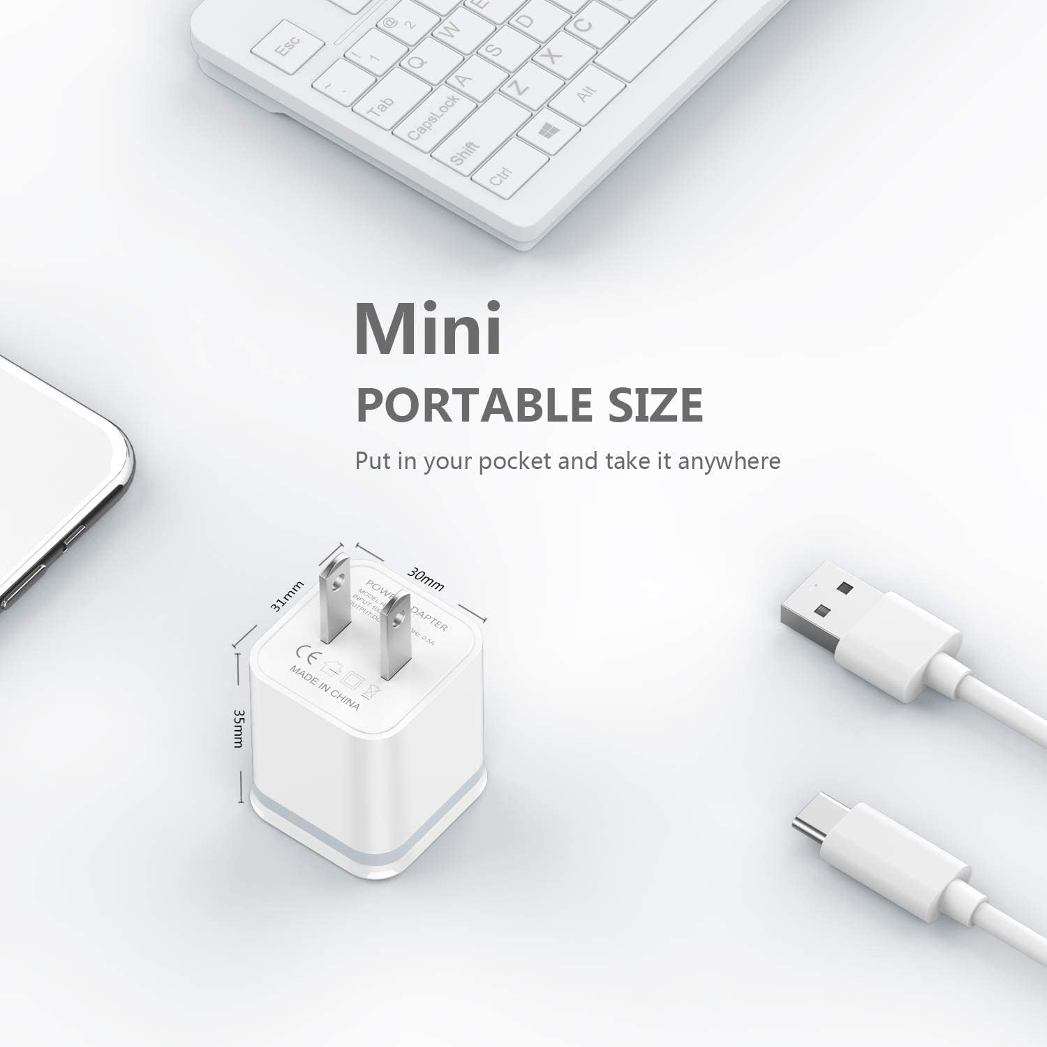White mini USB charger with dimensions, surrounded by a keyboard, phone, and cables.